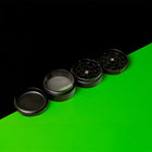 Offener Keramik Grinder Hybrid mit allen vier Teilen auf schwarzem und grünem Hintergrund.