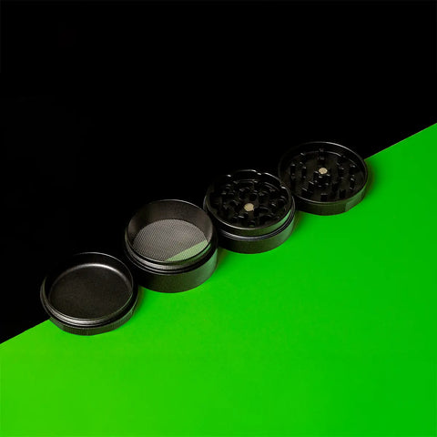 Offener Keramik Grinder Hybrid mit allen vier Teilen auf schwarzem und grünem Hintergrund.