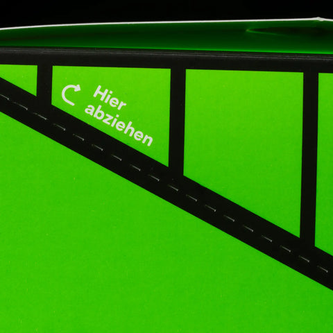 Detailaufnahme der perforierten Aufreißlinie am Hybrid Umkarton mit weißem Hinweis "Hier abziehen" und Pfeil-Symbol auf neongrünem Karton.